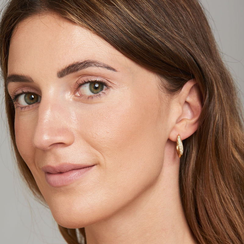 A delicate yet glamorous pair of gold earrings. These golden hoop earrings feature pave set topaz stone and its subtle wave design imbues you with elegance and sparkle. Team these gold earrings with the matching Athena Ear Cuff and an essential gold necklace from our collection.